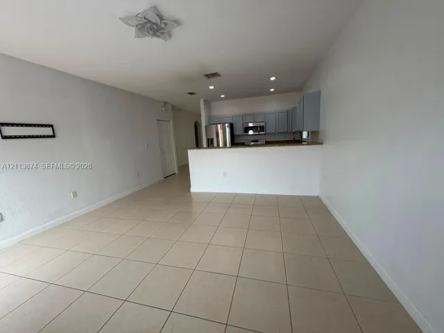 Open-concept interior featuring large-format tile flooring, recessed lighting, a breakfast bar, stainless steel appliances, and solid-color cabinetry