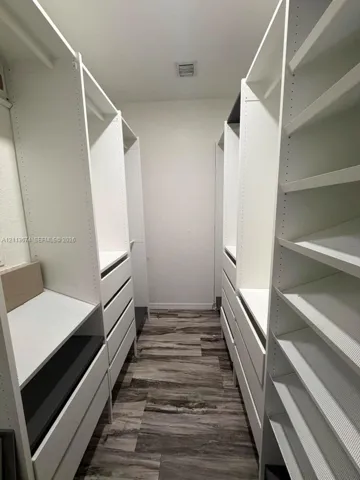 Walk-in closet featuring white built-in shelving, integrated storage drawers, hanging rods, and wood-finish flooring
