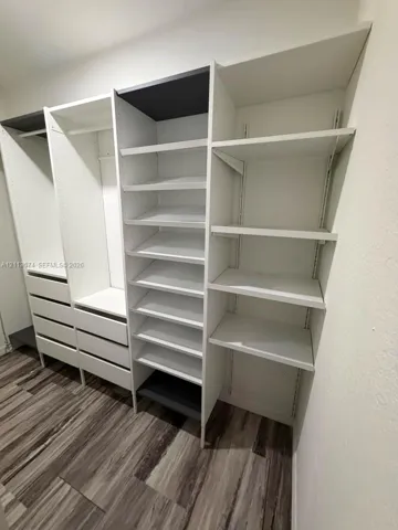 Custom storage system featuring floor-to-ceiling white shelving, integrated drawers, hanging rods, and wood-finish flooring