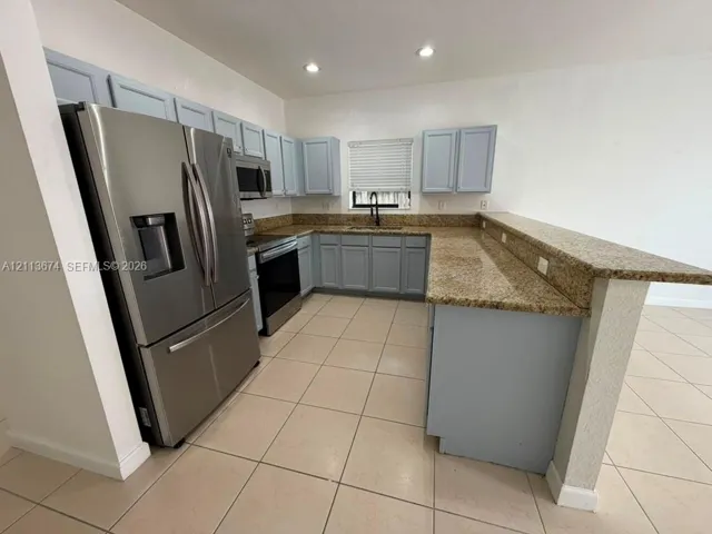 Kitchen featuring light blue cabinetry, stone-finish countertops, stainless steel appliances, tile flooring, and a breakfast bar