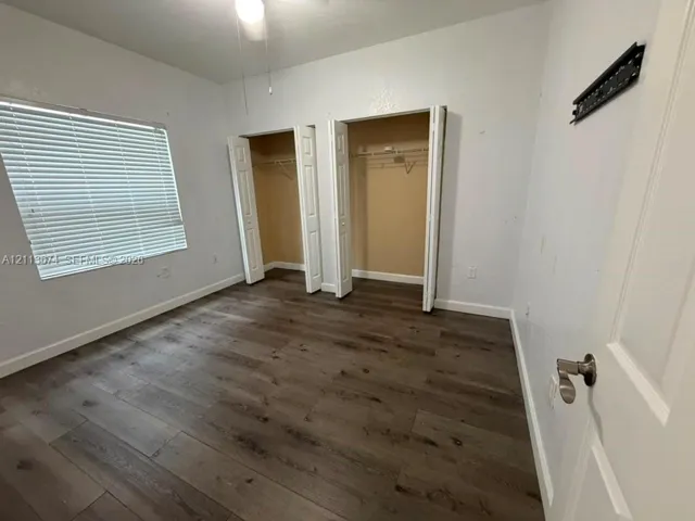 Interior room featuring wood-finish flooring, two closets with bi-fold doors, and a window with horizontal blinds