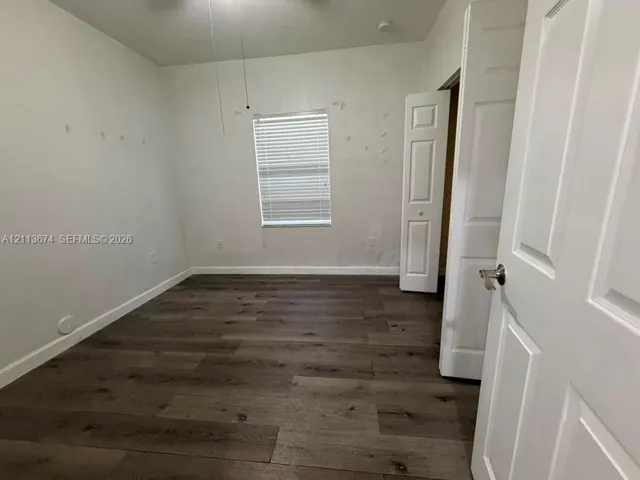 Room featuring wood-finish flooring, a single-panel window with horizontal blinds, and two six-panel interior doors with metallic lever handles