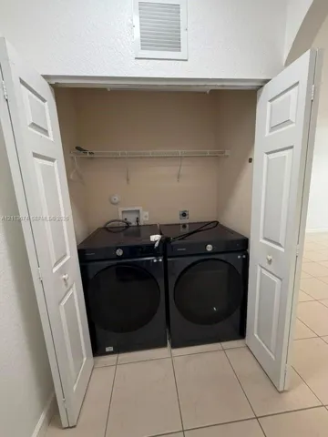 Laundry alcove featuring white bi-fold doors, tile flooring, and integrated overhead wire shelving