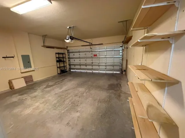 Multi-car garage featuring a concrete floor, sectional overhead door, built-in wall-mounted shelving, and overhead lighting