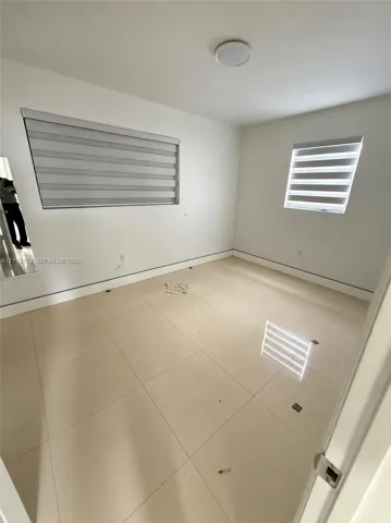 Neutral interior featuring large-format ceramic tile flooring, dual-layered roller shades, and a ceiling-mounted flush light fixture