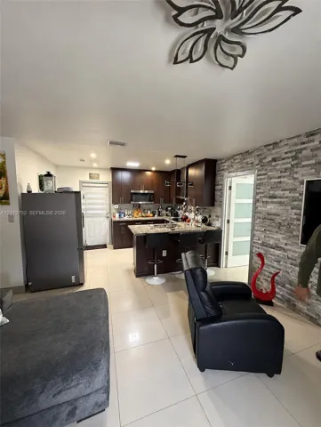 Kitchen featuring dark wood cabinetry, stone-finish countertops, stainless steel appliances, stacked-stone accent wall, and porcelain tile flooring