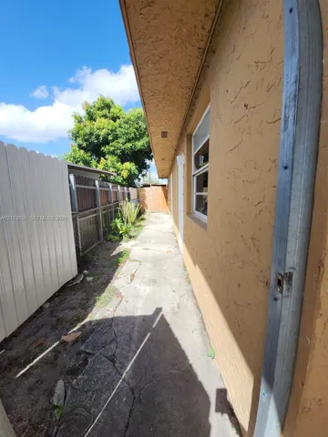 Side exterior featuring textured stucco siding, concrete path, and perimeter vinyl fencing