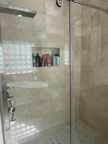 Walk-in shower featuring natural stone wall tile, built-in recessed wall niche, rainfall shower head, glass-block window, and pebble-style floor tile