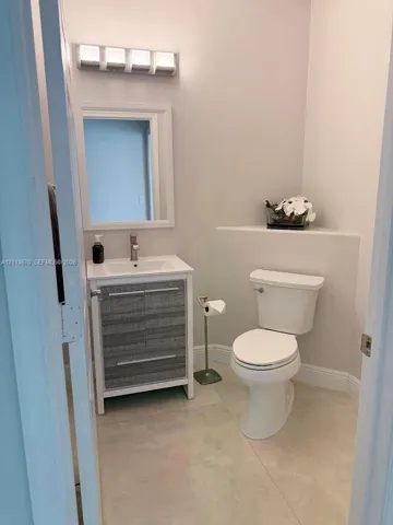 Vanity featuring a textured grey cabinet base, rectangular basin, and single-handle faucet, paired with a white-framed mirror, four-light vanity fixture, and neutral stone-finish tile flooring