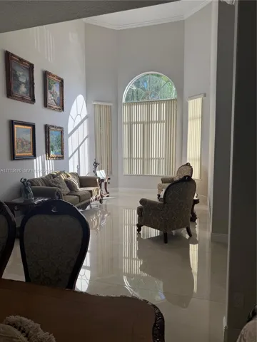 High-ceilinged living area featuring large-format polished tile flooring, an expansive arched window, and neutral wall tones