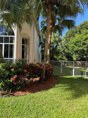 Stucco exterior featuring arched windows, mature palm trees, manicured lawn, and metal perimeter fencing