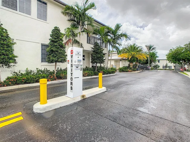 Gated vehicular entrance featuring an electronic access kiosk, asphalt drive, and landscaped grounds