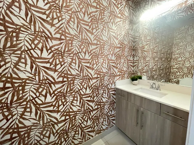 Wallpaper featuring a botanical print, flat-panel vanity with wood-finish cabinetry, solid-surface countertop, rectangular undermount sink, and polished chrome dual-handle faucet