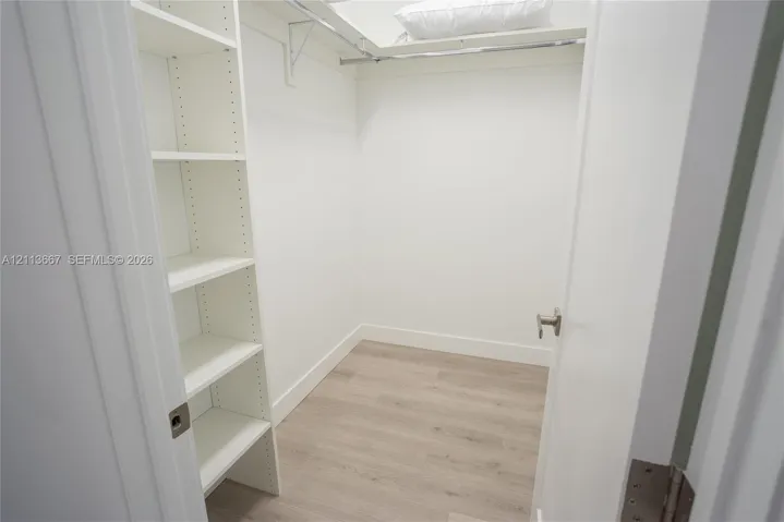 Walk-in closet featuring white built-in shelving, wood-finish flooring, and a metal garment rod