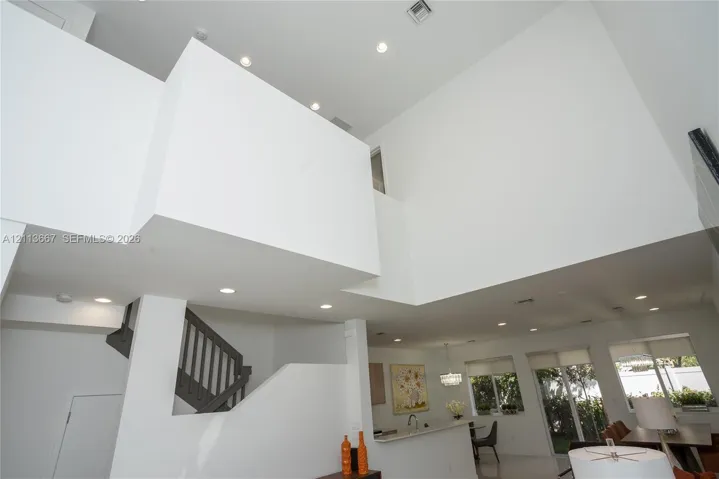 Double-height volume ceiling, recessed lighting, and staircase with dark-toned balustrades