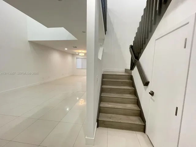Staircase featuring wood-finish treads and a dark-toned railing, complemented by large-format tile flooring and recessed lighting
