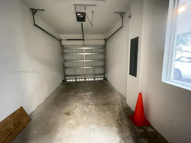 Single-car garage featuring a roll-up metal door, concrete flooring, smooth wall finishes, and an integrated electrical panel