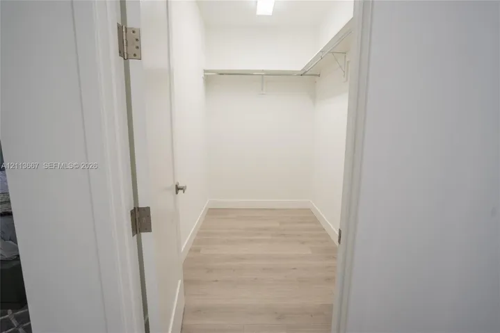 Walk-in closet featuring wood-finish flooring, white walls, and built-in shelving with an integrated clothes rod