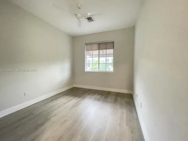 Neutral-toned interior featuring wood-finish flooring, a multi-pane window with a roller shade, and a ceiling-mounted fan