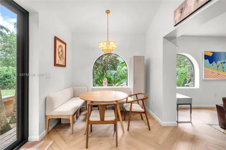 Herringbone wood-finish flooring, vaulted ceilings, multi-tiered brass pendant lighting, and arched windows with exterior greenery
