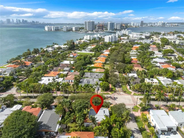 Aerial perspective of a coastal residential neighborhood featuring mature palm trees, proximity to waterfront, paved streets, and a dense canopy of foliage