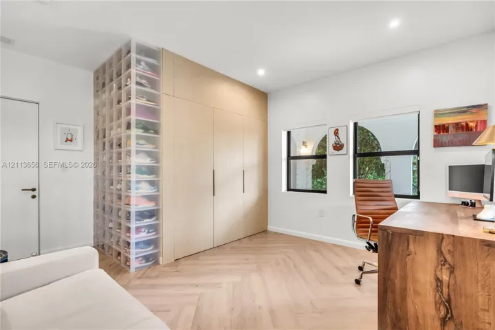 Floor-to-ceiling built-in cabinetry with flat-panel doors, herringbone-pattern wood-finish flooring, recessed lighting, and dual windows with black frames