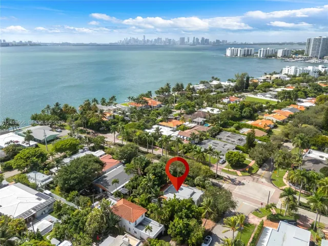 Aerial perspective of a coastal residential area featuring mature landscaping, proximity to the waterfront, and a skyline backdrop