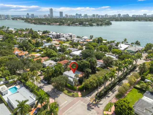 Aerial perspective of a coastal property featuring mature palm trees, dense perimeter landscaping, and a flat roofline