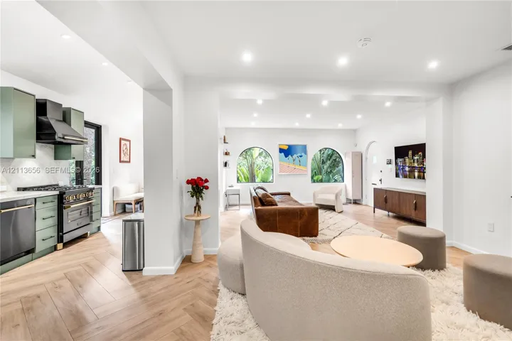 Herringbone wood-finish flooring, recessed lighting, arched windows, matte sage cabinetry, and professional-style range with integrated hood