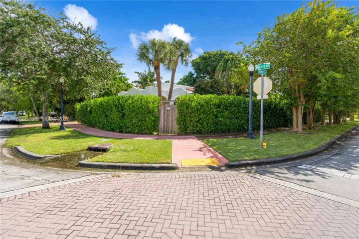 Corner lot property featuring mature landscaping, dense privacy hedging, and palm trees with a gated wood entryway