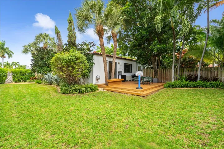 Private backyard featuring a wood-finish deck, mature palm trees, lush landscaping, and perimeter wood fencing