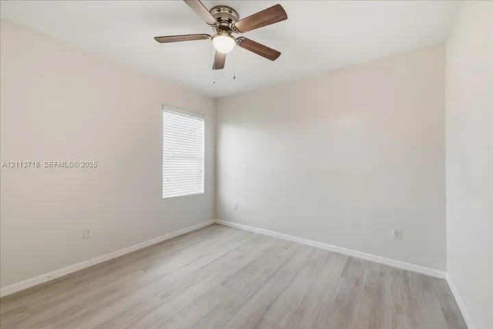 Neutral-toned interior room featuring wood-finish flooring, a ceiling fan with integrated lighting, and a window with blinds