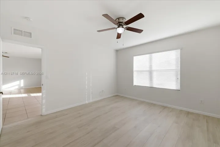 Neutral interior featuring wood-finish flooring, a ceiling fan with integrated lighting, and a window with horizontal blinds