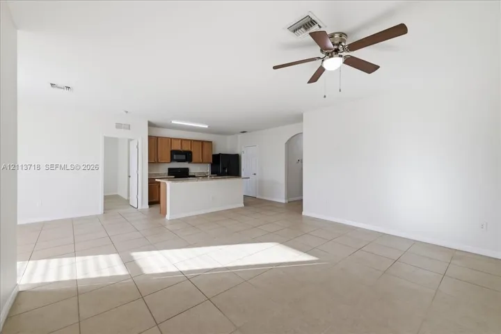 Open floor plan featuring large-format tile flooring, a kitchen breakfast bar, wood cabinetry, and a ceiling fan with integrated light fixture