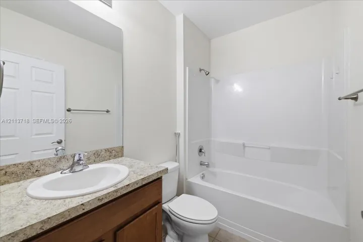 Full bathroom featuring a wood-finish vanity, stone-patterned countertop, oval under-mount sink, and a combination tub and shower enclosure with a wall-mounted fixture