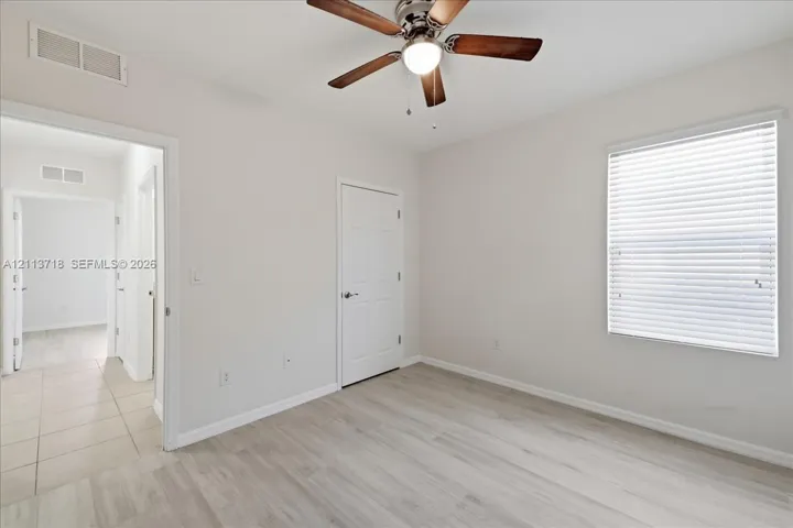 Neutral interior featuring light wood-finish flooring, ceiling fan with integrated lighting, and horizontal window blinds