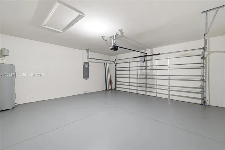 Attached garage featuring painted masonry walls, sealed flooring, an automated overhead door, and a ceiling-mounted access panel
