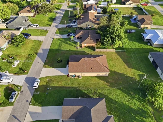 Aerial perspective of a single-story residence featuring a shingled roof, concrete driveway, and a fenced lot