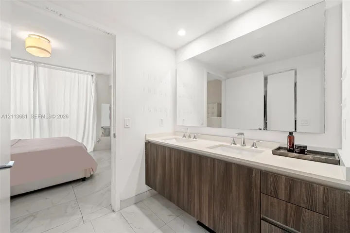 Double vanity with a composite countertop, dual rectangular undermount sinks, wood-finish cabinetry, a large wall-mounted mirror, and light-toned tile flooring