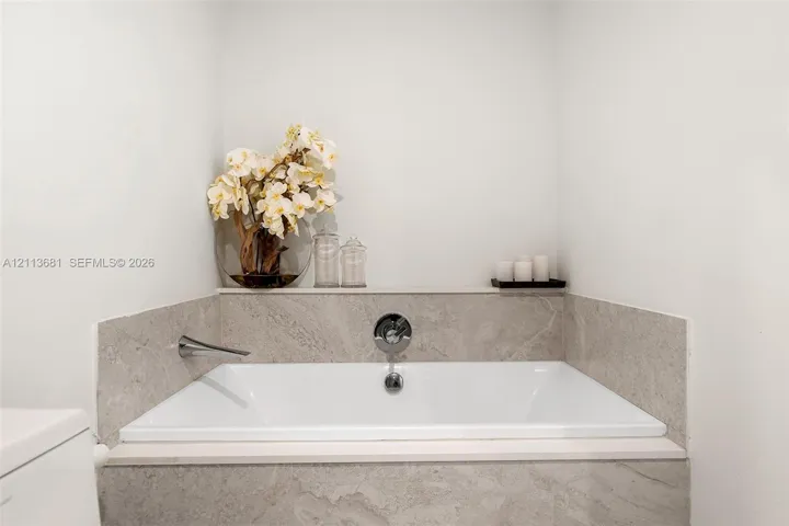 Built-in soaking tub featuring large-format stone surround, wall-mounted faucet, and integrated stone deck