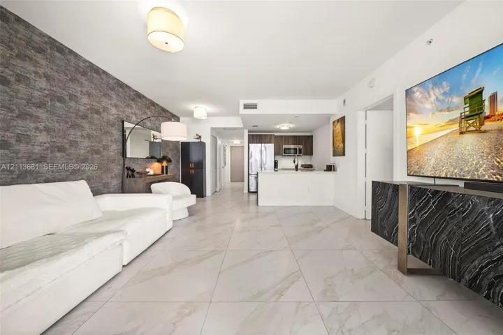 Open-concept interior featuring large-format tile flooring, a textured stone-finish accent wall, and recessed lighting