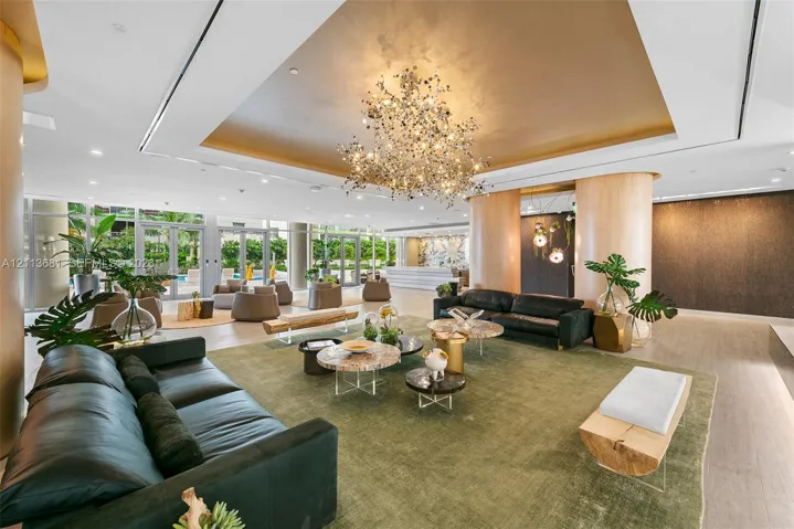 Expansive lobby featuring a recessed gold-leaf tray ceiling, artistic sculptural chandelier, floor-to-ceiling glass wall, and rounded wooden support columns
