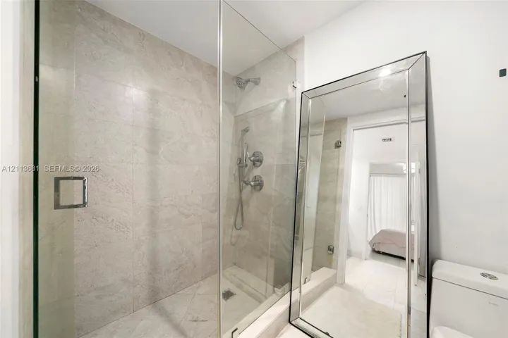 Walk-in shower featuring glass paneling, floor-to-ceiling stone-finish tile, and polished chrome hardware