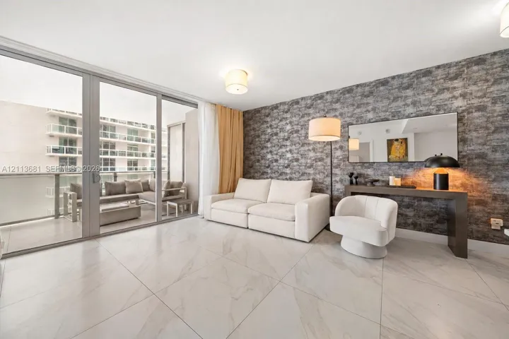 Living area featuring oversized floor-to-ceiling glass sliding doors, stone-finish tile flooring, and a textured stone-look accent wall