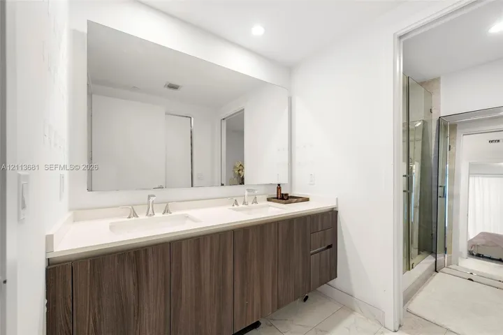 Floating dual-sink vanity with dark wood-finish cabinetry, solid surface countertops, polished chrome widespread faucets, and a large wall-mounted mirror