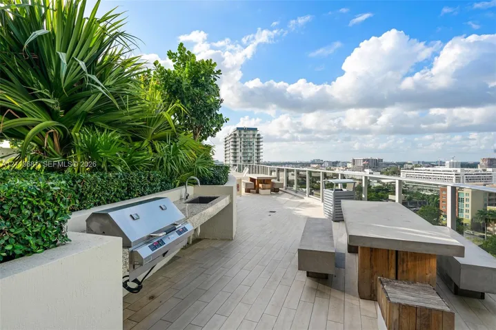 Rooftop terrace featuring tile flooring, built-in stainless steel grill, stone-surface countertop with integrated sink, concrete dining elements, and glass panel railing