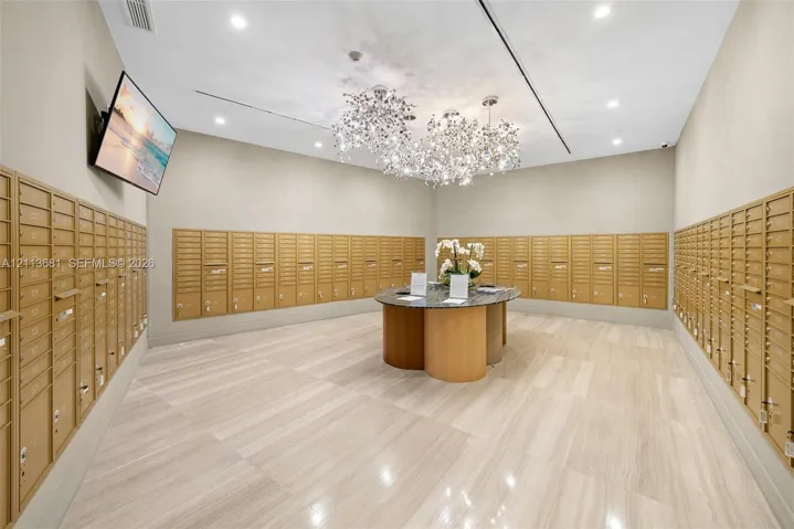 Mail room featuring wall-to-wall metallic postal lockers, stone-top center island, recessed ceiling lighting, decorative cluster chandeliers, and polished tile flooring