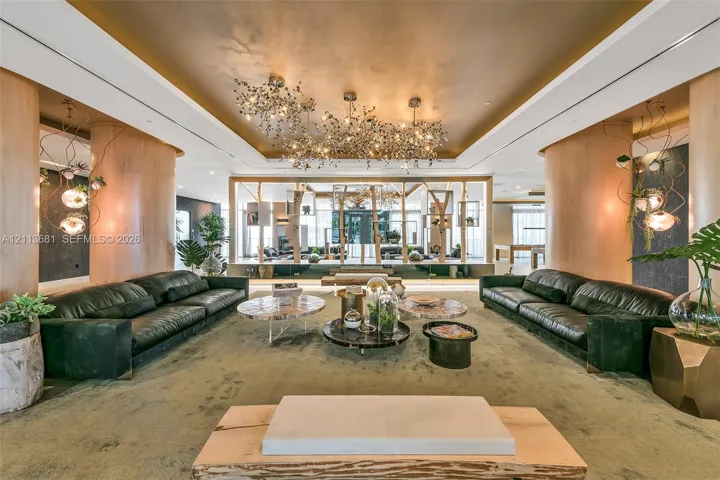 Expansive room featuring a recessed tray ceiling with gold-toned finish, intricate cluster chandeliers, curved wood-paneled structural columns, and an open timber-framed partition