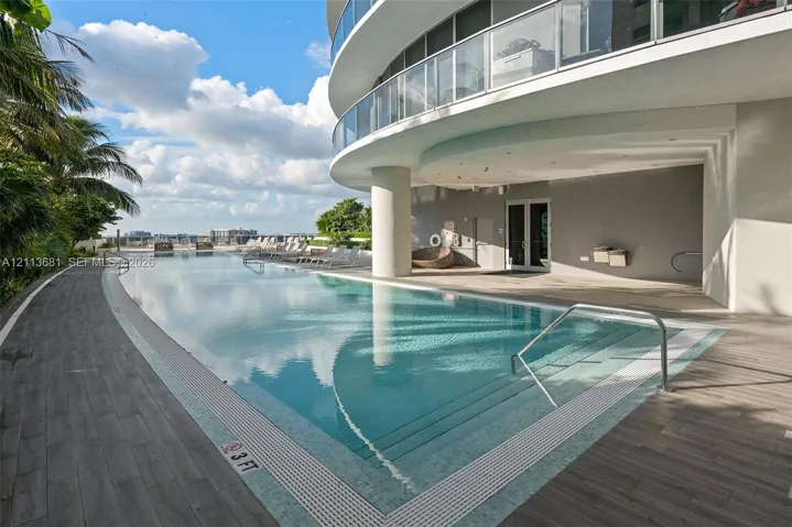 Curved swimming pool featuring a tile border, metal handrails, integrated steps, and wood-finish decking