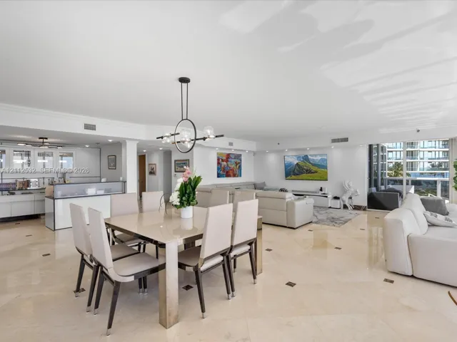 Open-concept interior featuring light-toned stone tile flooring with decorative inserts, floor-to-ceiling glass panel doors, modern geometric multi-light chandelier, and high-gloss white cabinetry